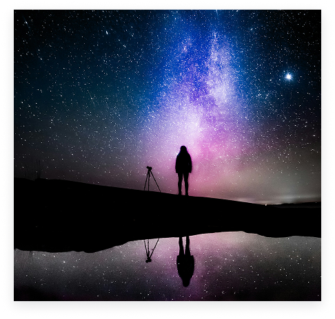 A photographer reflected beneath a colorful night sky